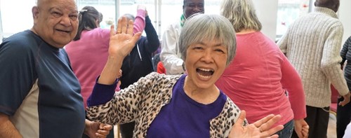 Photo from Claremont Project: At the forefront, an older woman smiles and dances, facing the camera.