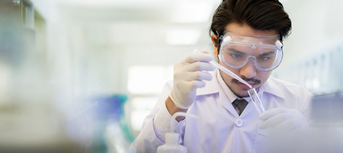 Photo from AAAMD: A young man conducts scientific research wearing goggles and a lapcoat.